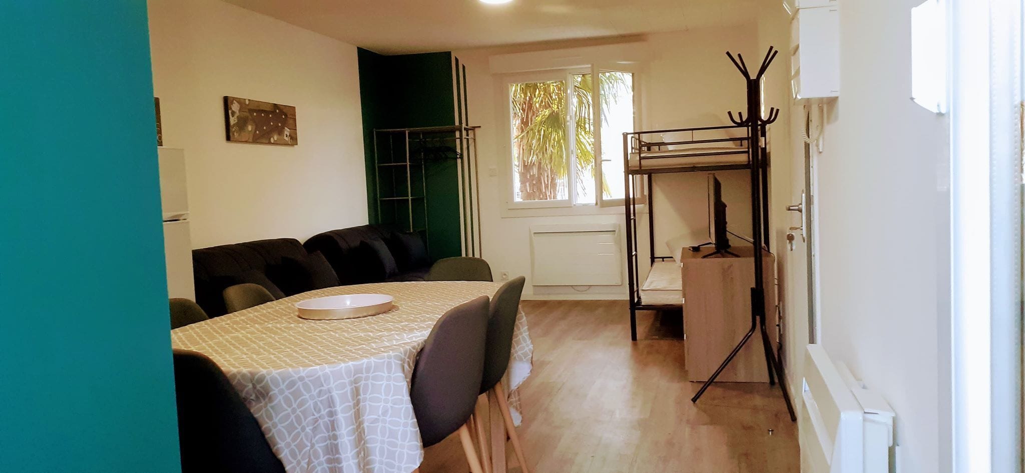 A dining area with a table set for four, a window with a view of palm trees, and a coat rack with a mirror.