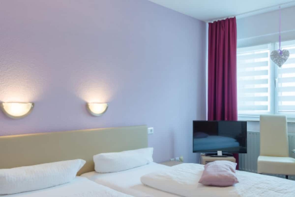 A hotel room with two beds, a TV, and a window with curtains.
