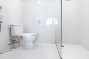Une salle de bain moderne équipée de toilettes, d’une douche et d’un espace douche clos par des parois de verre.