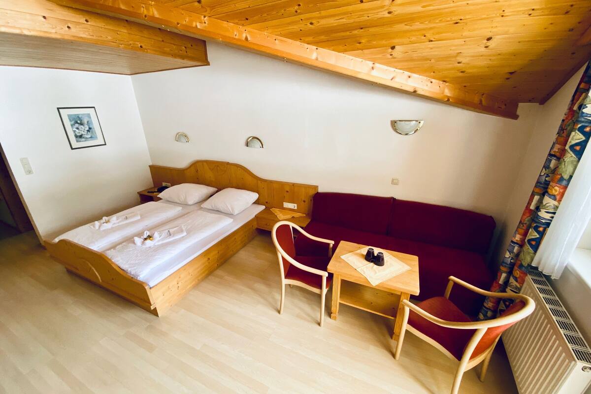 A bedroom with a wooden bed, a red sofa, a small table, and a chair.