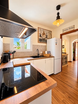 A modern kitchen with a black induction cooktop, white cabinetry, a black range hood, and a wooden countertop. - Casa Sol: Mediterranean Charm by the Sea (Cala d'Or)