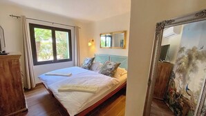 Un dormitorio con cama, mesita de noche, espejo y ventana con cortinas.