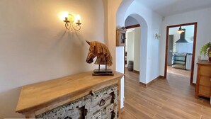 Un pasillo con una consola de madera, una escultura de cabeza de caballo montada en la pared, y un aplique.