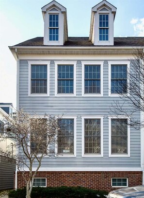 Une maison à deux étages, avec des fondations en briques, de nombreuses fenêtres et un petit arbre dans le jardin.