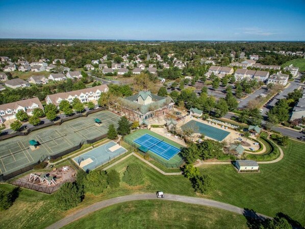 Vue aérienne d’un quartier résidentiel avec des maisons, un court de tennis et une piscine.