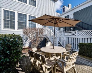 Une terrasse en bois avec une table ronde et des chaises, un parasol et une clôture blanche en bois.
