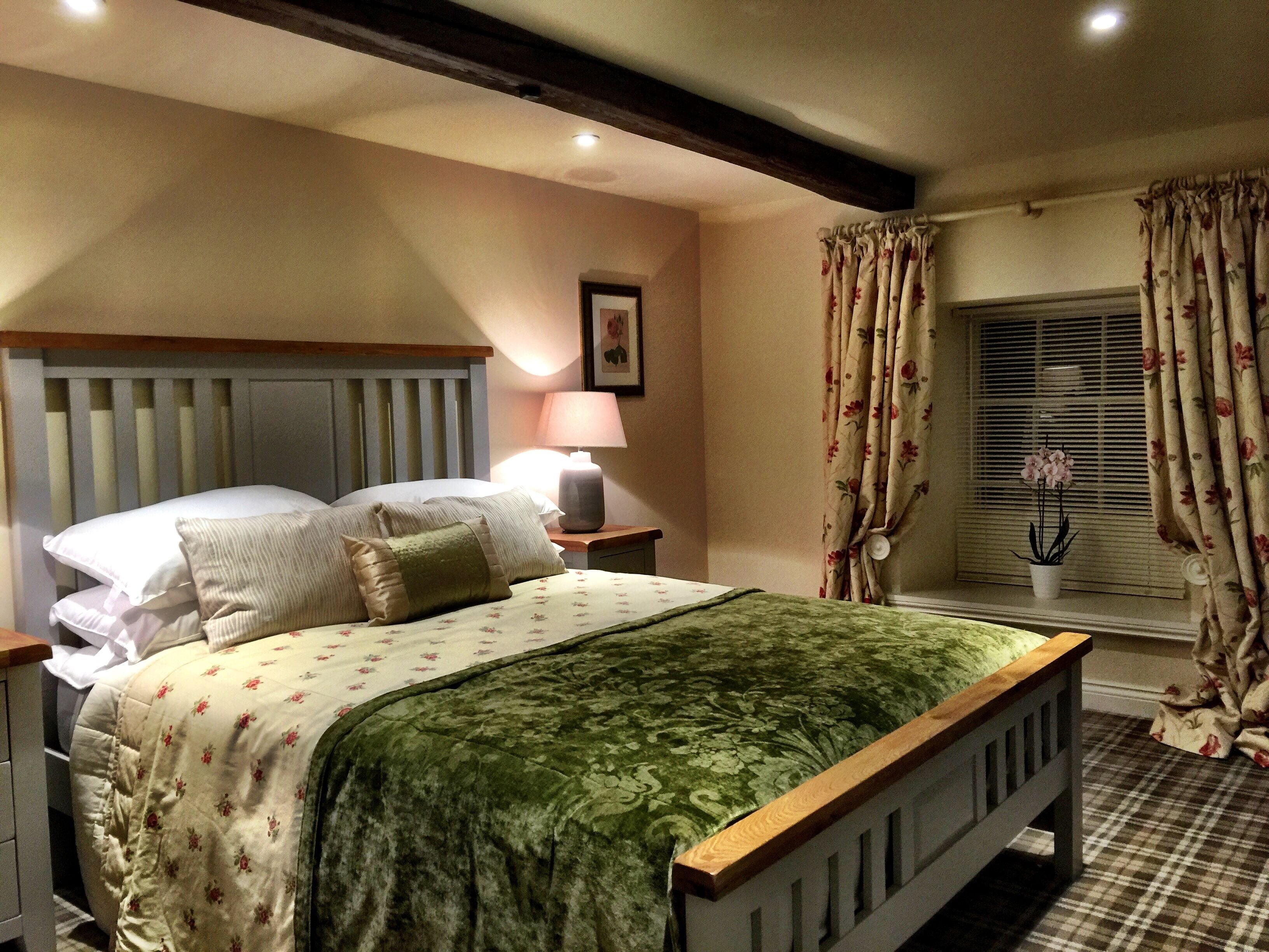 Une chambre à coucher avec un lit, des tables de chevet, une lampe, des rideaux à motifs floraux et une fenêtre avec des stores.