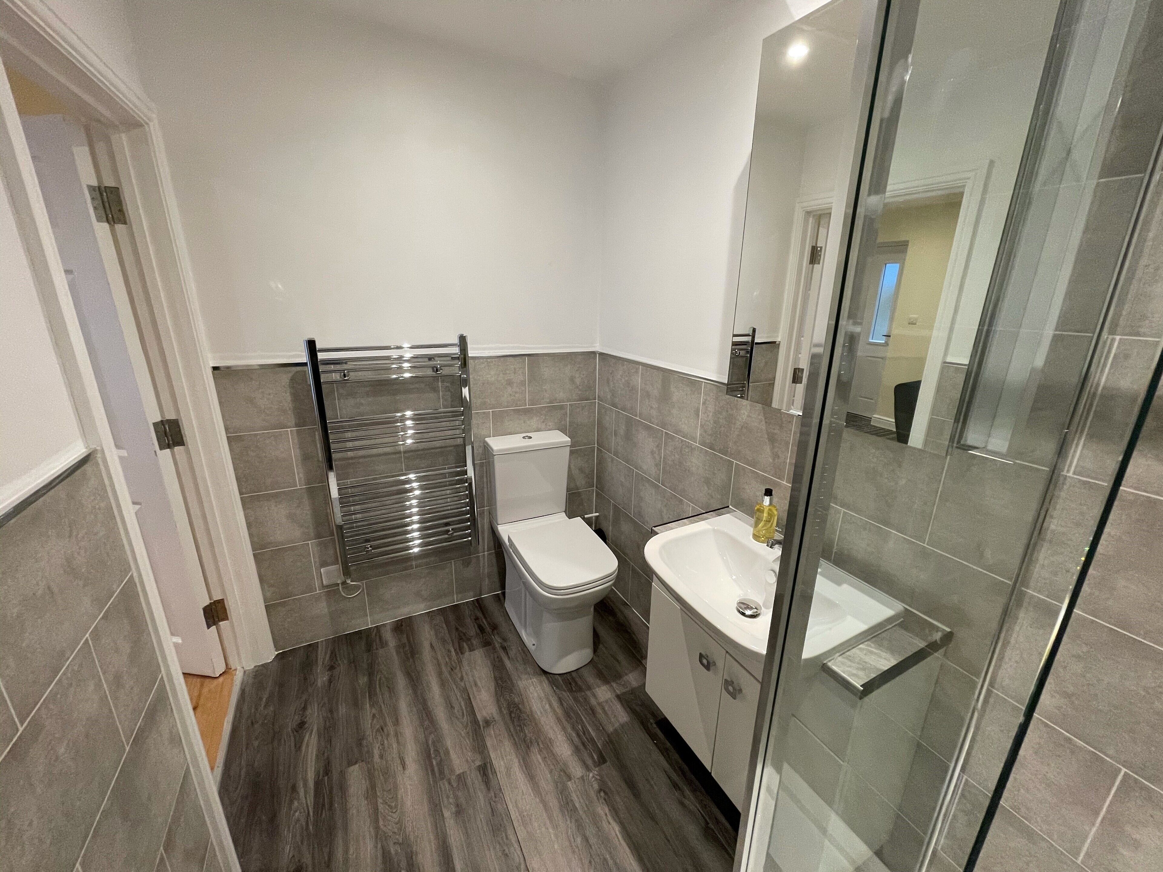 A modern bathroom with a glass shower enclosure, a white toilet, and a sink with a mirror above it.