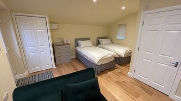 A compact bedroom with two single beds, a dresser, a green sofa, and a window with blinds.