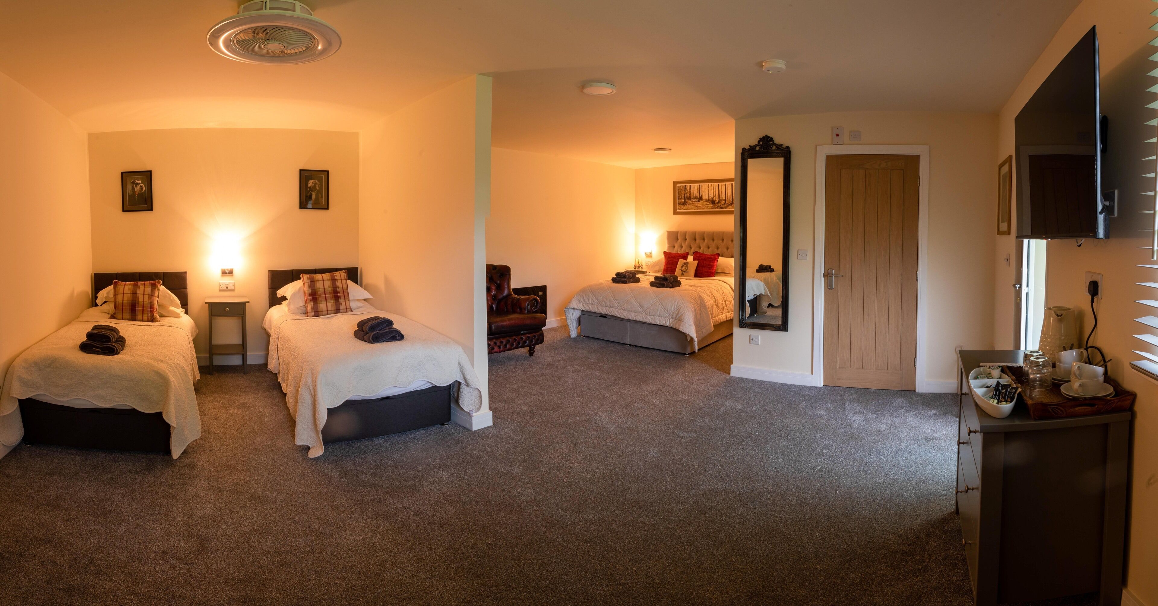 Habitación de hotel con dos camas, zona de estar, espejo grande, televisor y pequeña kitchenette.