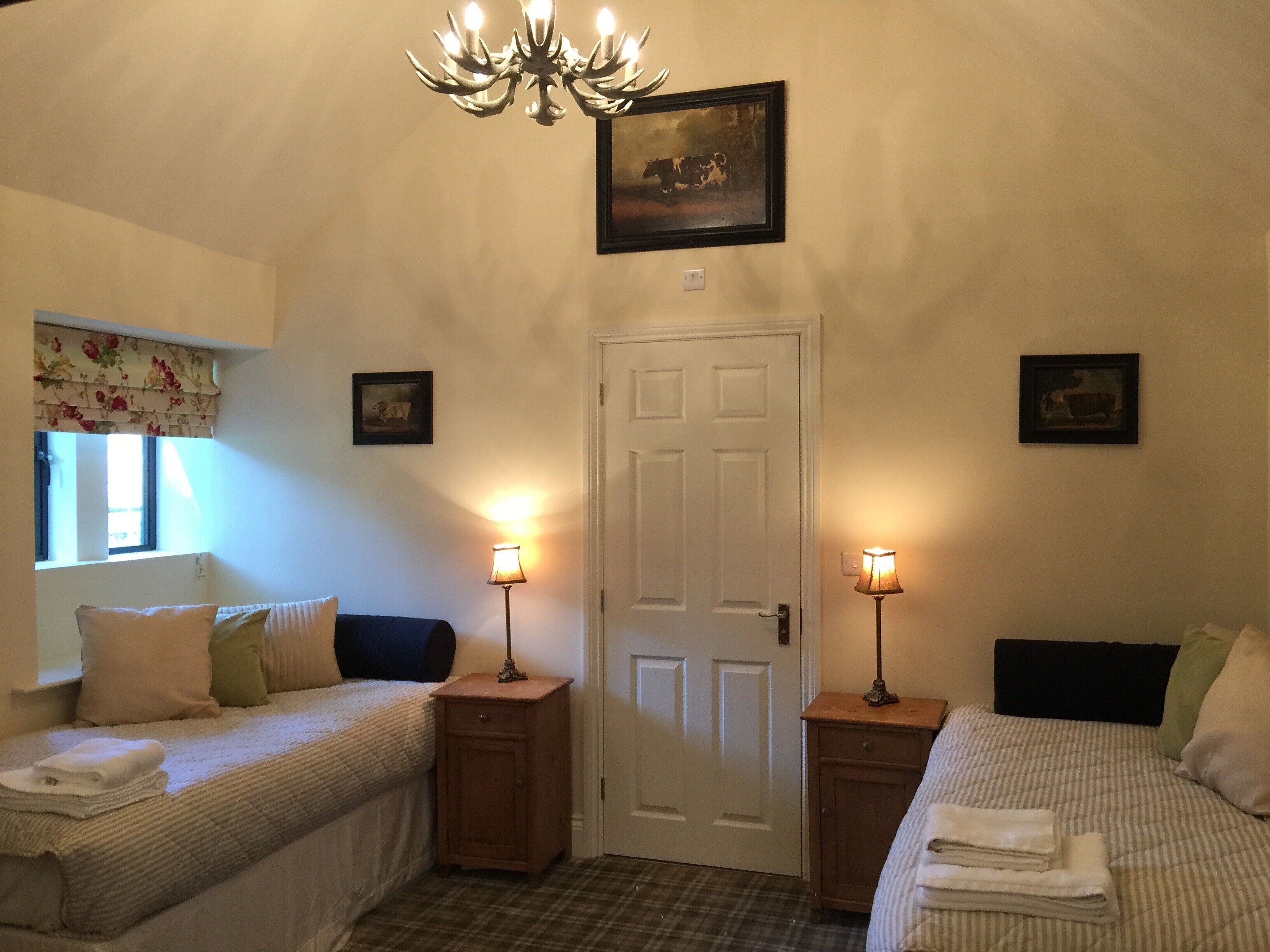 A bedroom with two beds, a chandelier, and two bedside tables with lamps.