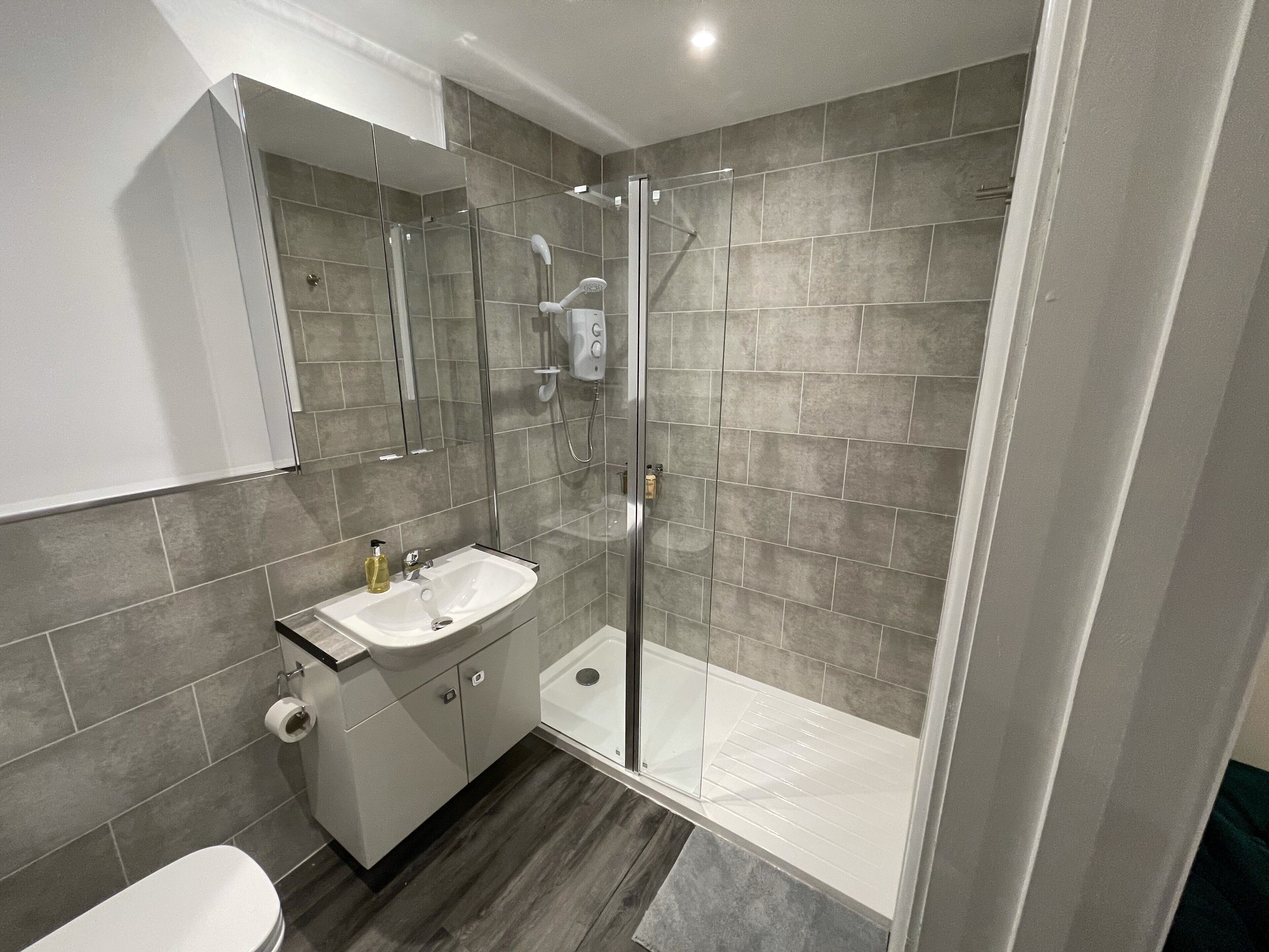 Une salle de bain moderne avec une douche à parois de verre, un lavabo blanc et un miroir au-dessus.