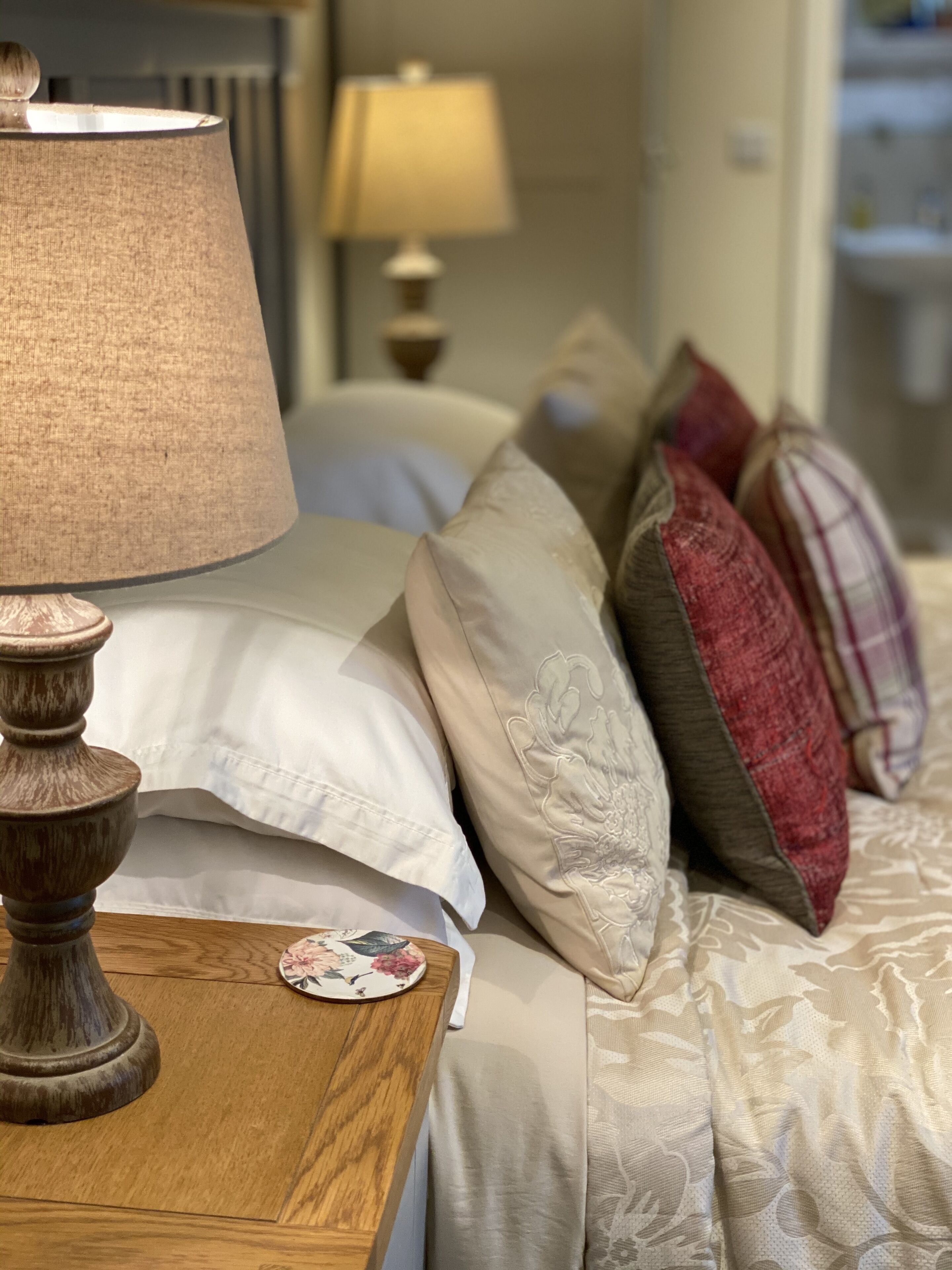 A neatly made bed with a wooden nightstand beside it, featuring a lamp and a decorative plate.