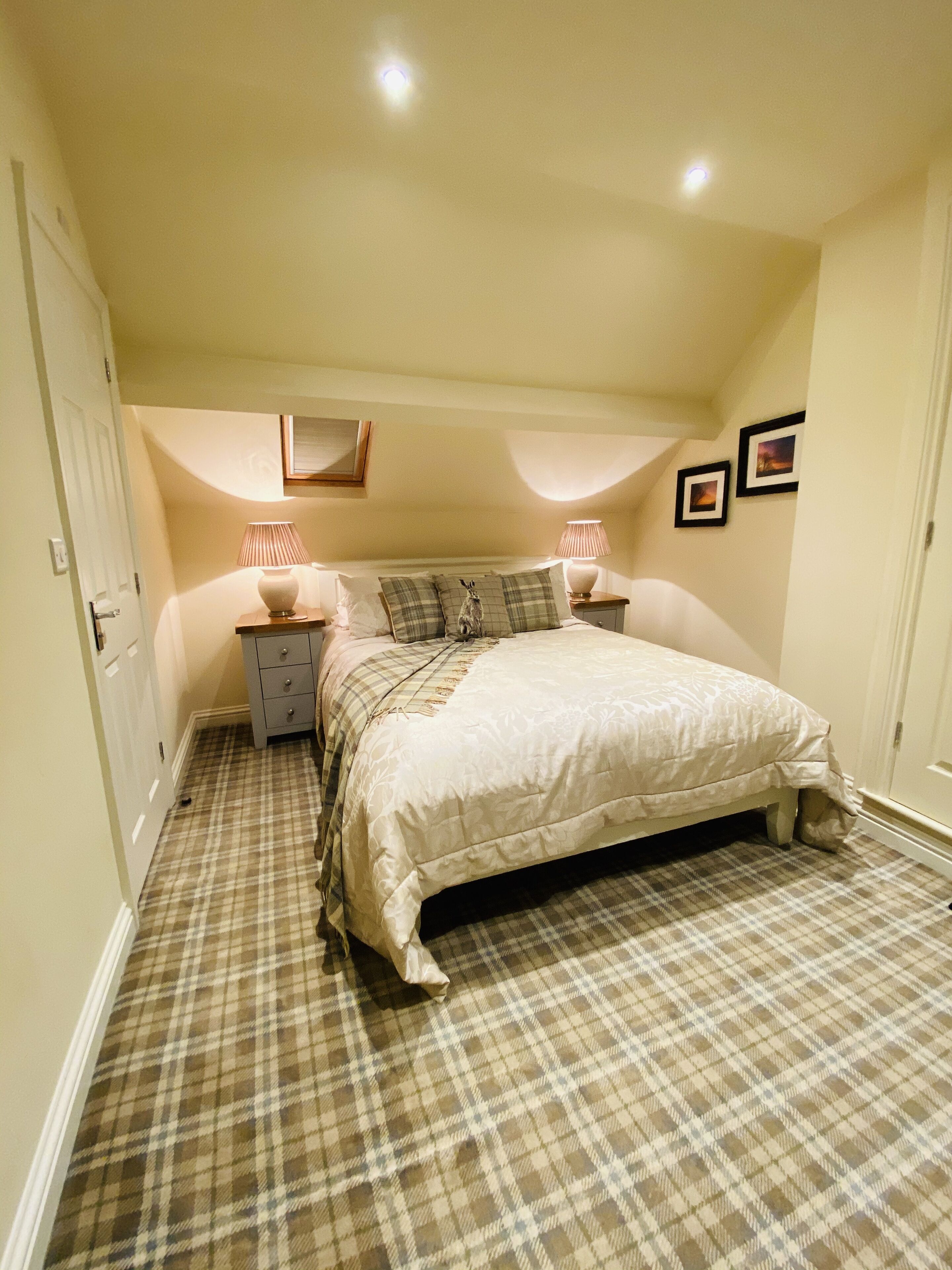Une chambre à coucher avec un lit, des tables de chevet, une lampe, un miroir et deux tableaux encadrés accrochés au mur.