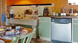 Una cocina con lavaplatos, estufa y lavavajillas. Hay una mesa con platos y tazas.