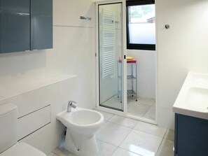 Een moderne badkamer met toilet, bidet en een douchecabine met glazen wanden.