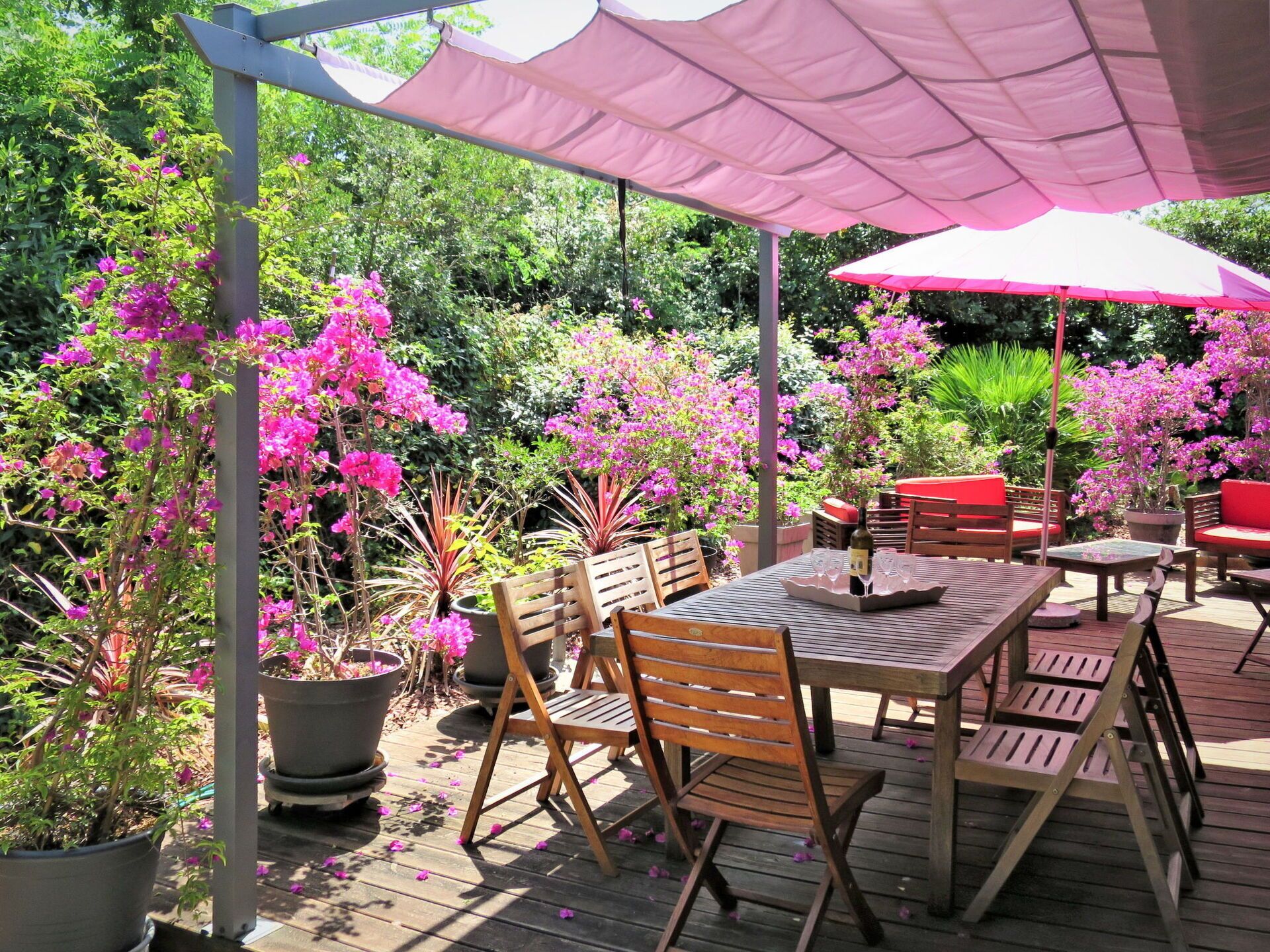 Une terrasse extérieure avec des meubles en bois, une table avec des verres à vin et des plantes en pot.