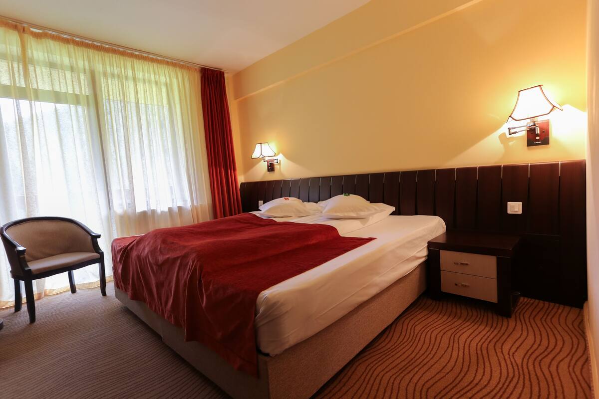 A hotel room with a bed, a chair, a nightstand, and two wall lamps.