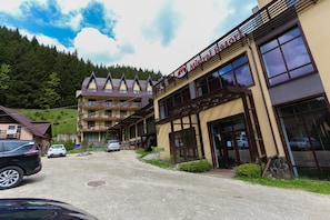 A hotel with a mountain backdrop, a parking area, and a building with large windows.