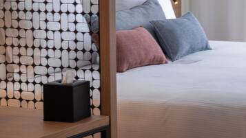 Una cama bien hecha con cabecera de madera, una mesita de noche con un dispensador de pañuelos de papel y un separador de ambientes con diseño.
