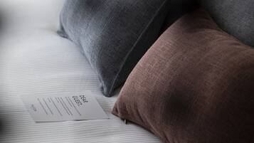 Una cama con sábana blanca y tres almohadas en distintos tonos.