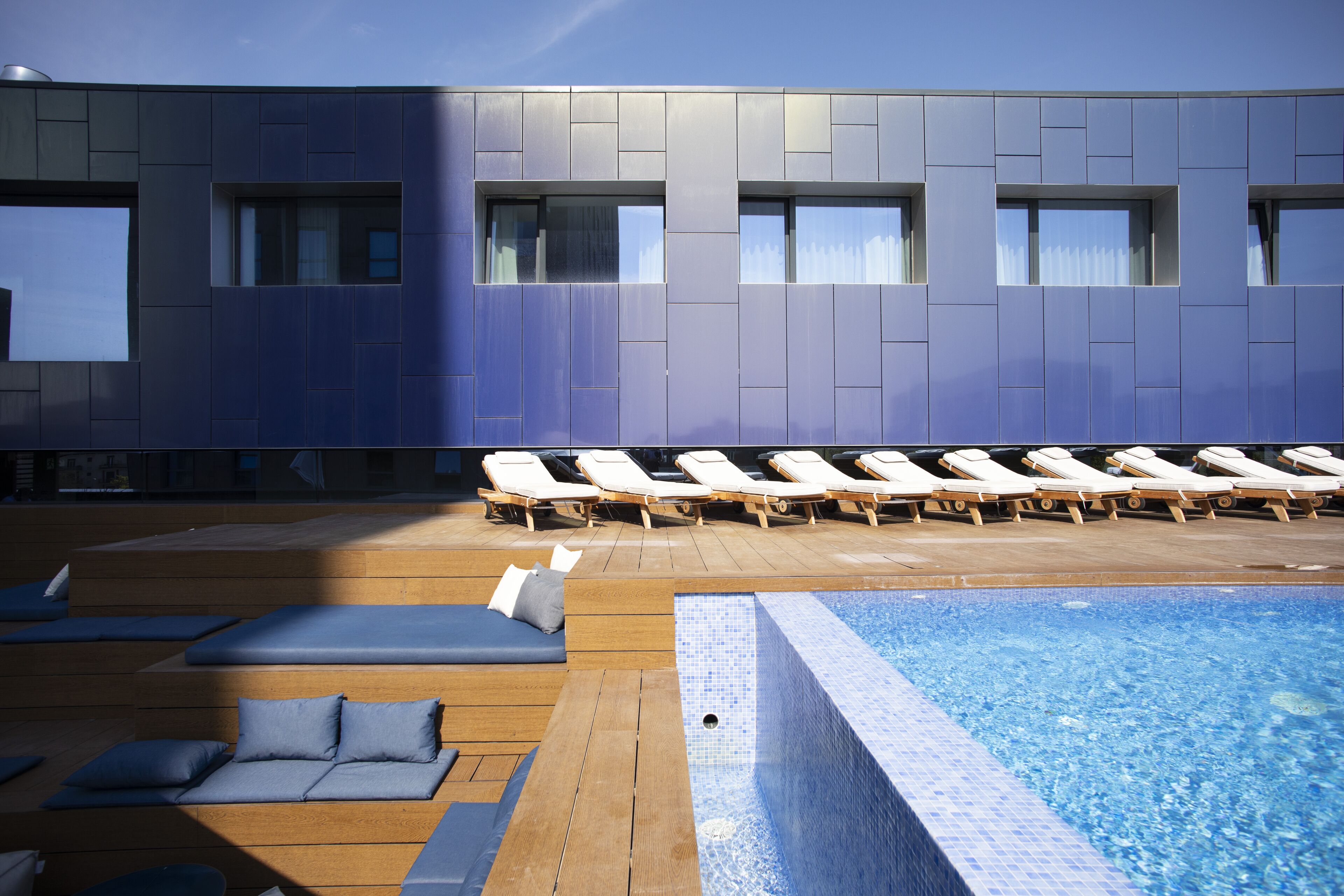 Un área de piscina interior moderna con sillones de descanso y asientos de madera.