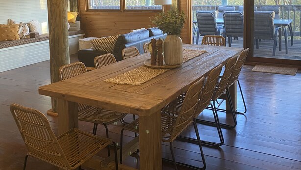 Een ruime eetruimte met een lange houten tafel, rieten stoelen en hangende hanglampen.