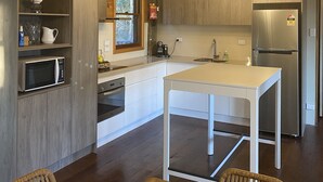 Een moderne keuken met houten kastjes, een roestvrijstalen koelkast, een witte tafel en een hanglamp.