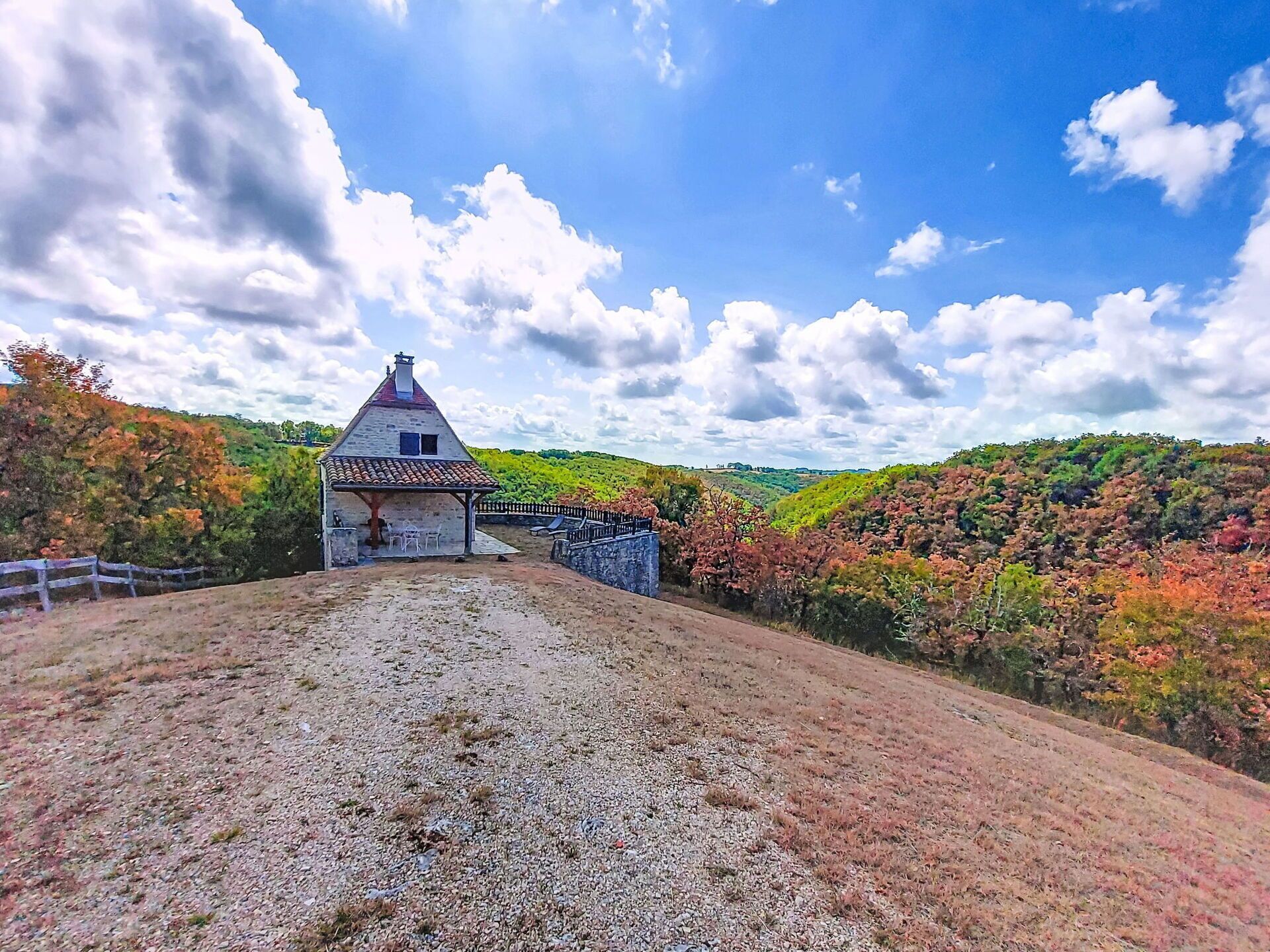 Ein rustikales Steinhaus mit Ziegeldach, umgeben von einem Kiesweg und einem Holzzaun.