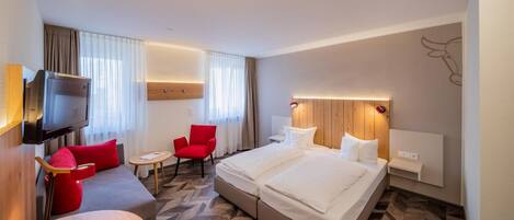 A hotel room with a bed, a TV, a sofa, and a chair.