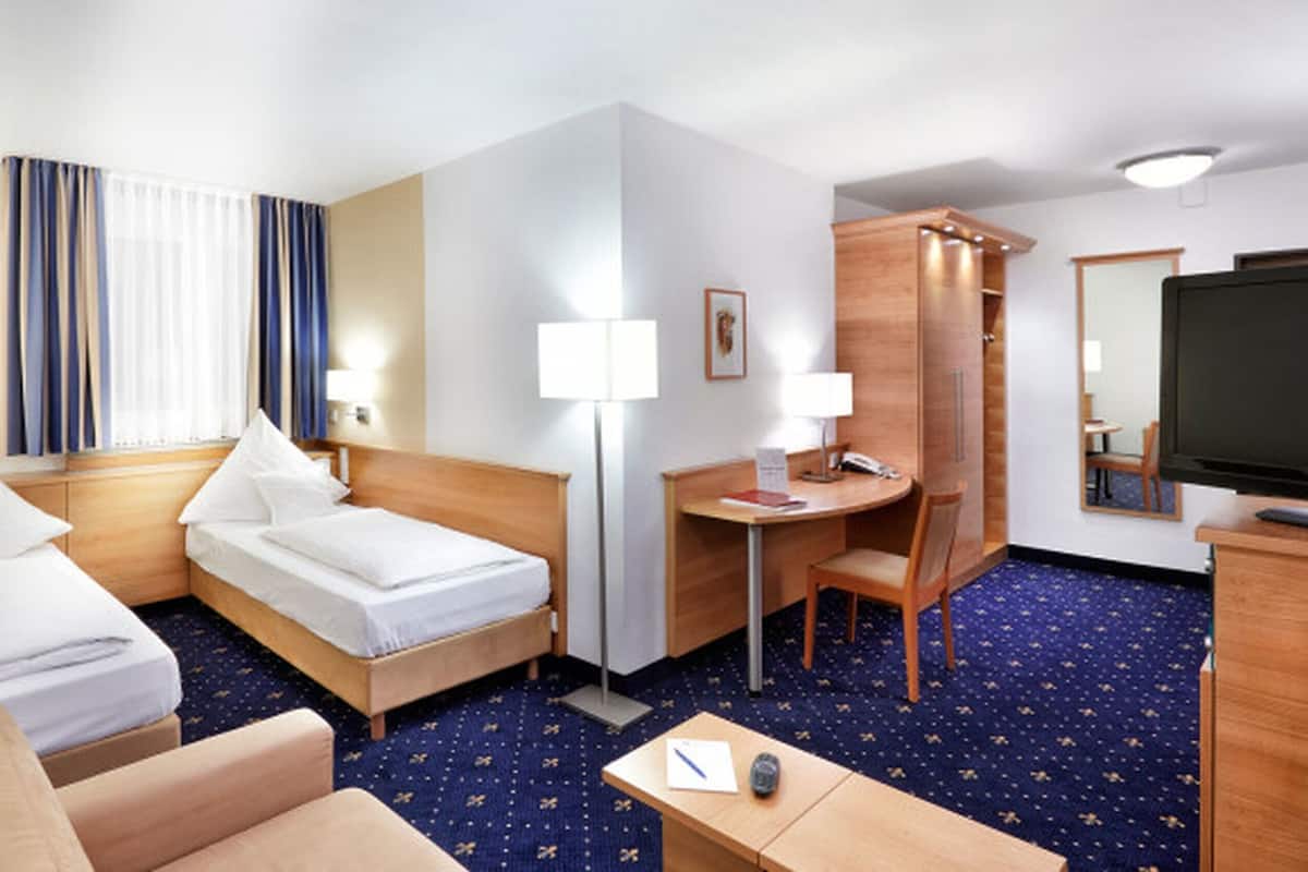 Habitació d'hotel amb dos llits individuals, una taula de treball amb cadira, una taula petita amb cadira, una televisió i un armari.