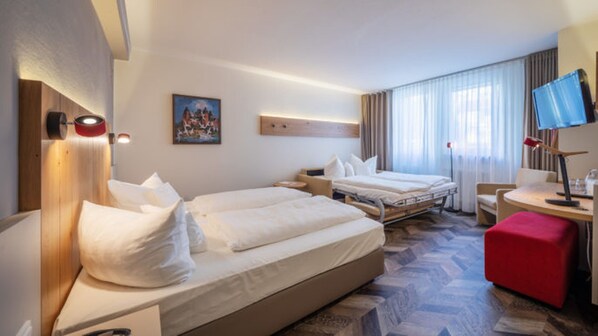 A hotel room with two beds, a desk with a chair, a TV, and a red ottoman. - Zum Goldenen Ochsen (Aschaffenburg)