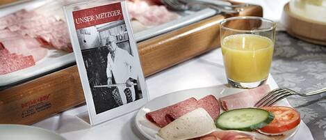 A breakfast setting with a plate of meats, cheese, and vegetables, a glass of orange juice, and a sign with a photo.