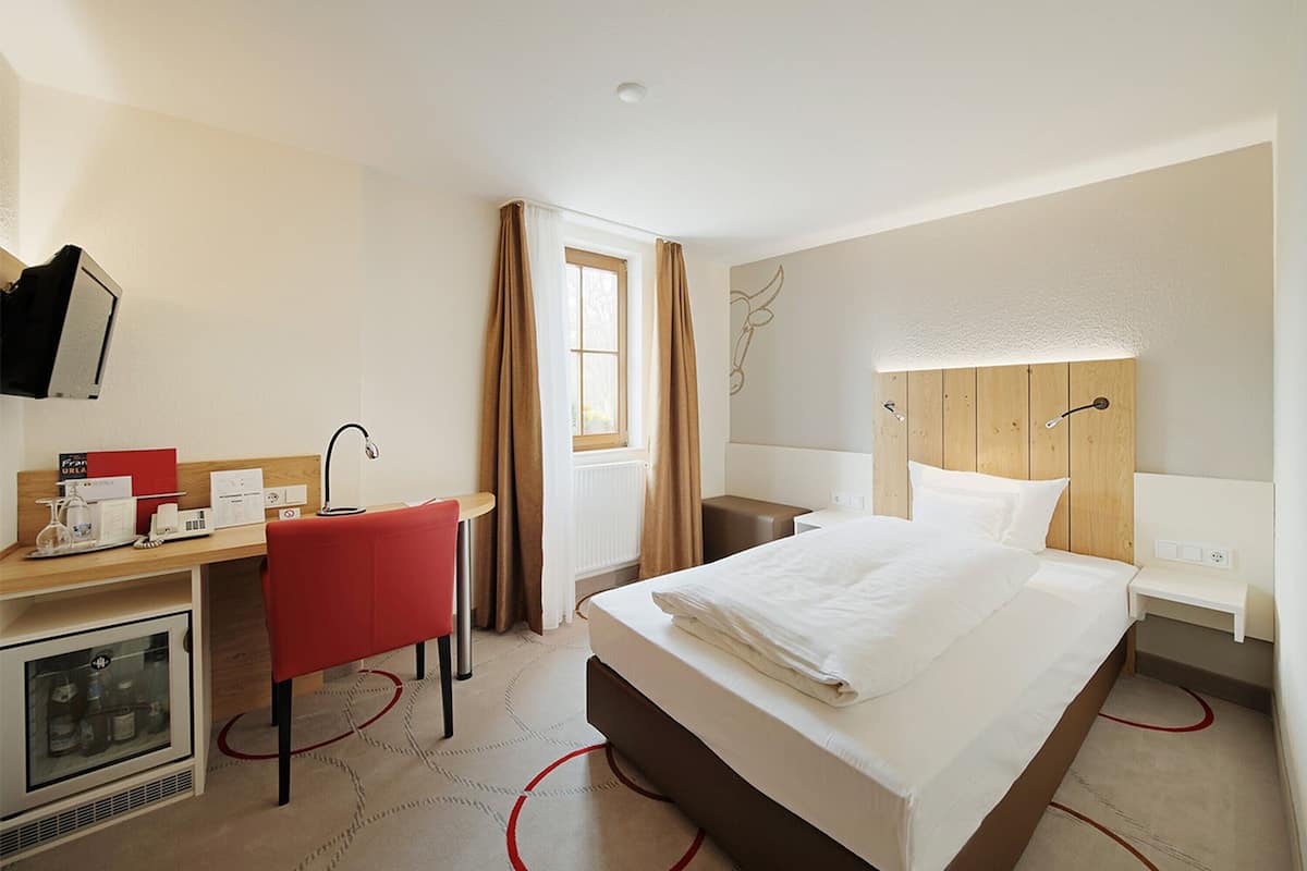 Habitació d'hotel amb un llit, una taula, una cadira, una televisió i un barreter.