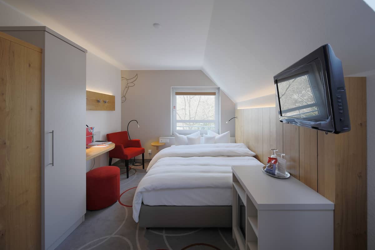 Habitació d'hotel moderna amb llit, escriptori, cadira, televisió i finestra.
