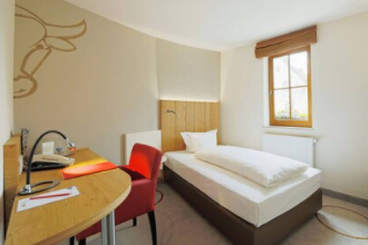 Habitació d'hotel amb llit, escriptori, cadira, televisió i finestra.
