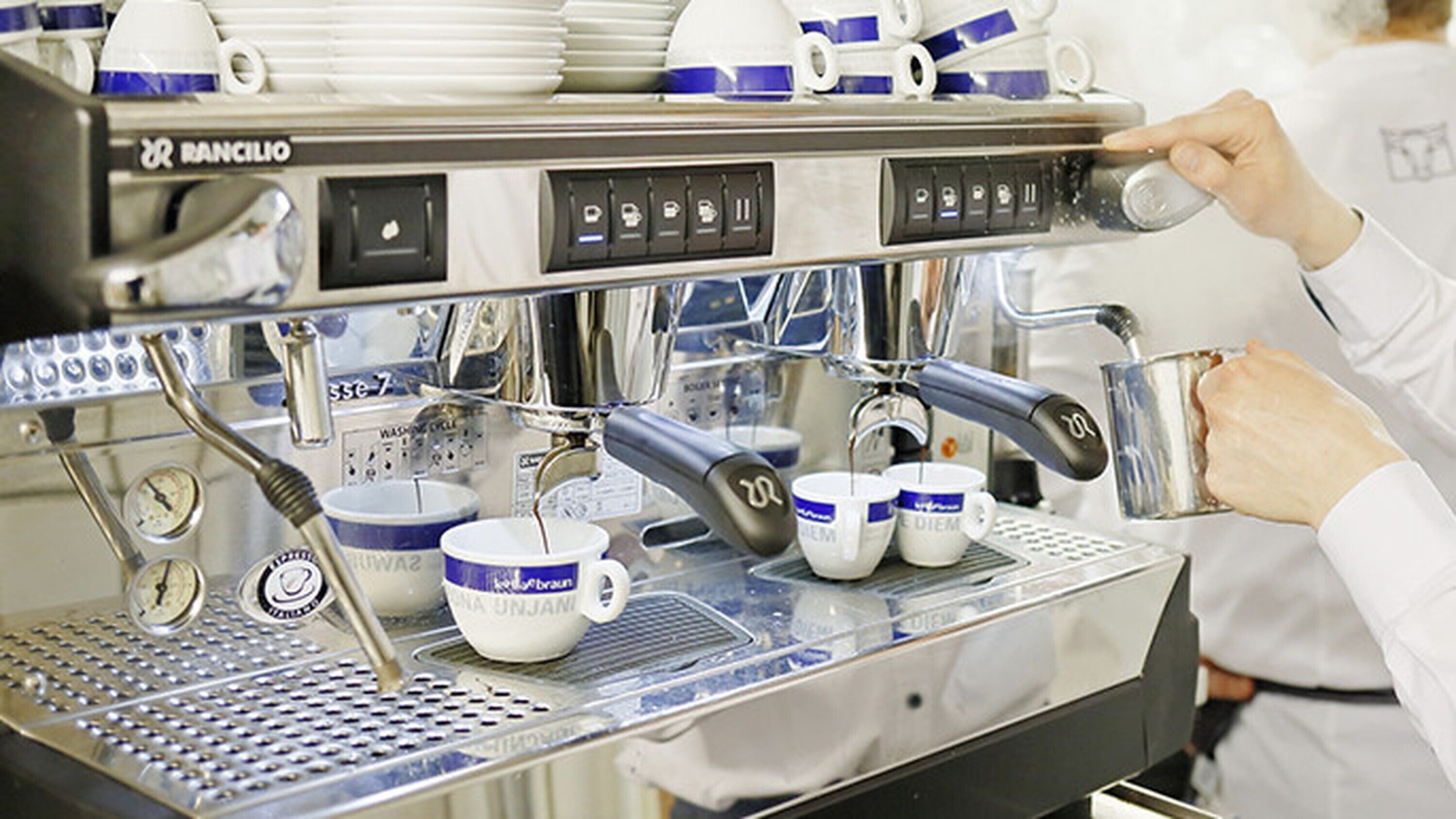 Een koffieapparaat met meerdere kopjes en een persoon die het bedient.