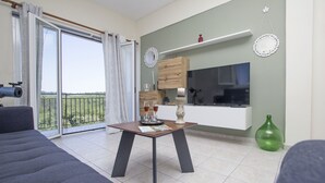 A modern living room with a sofa, a table with drinks, a TV, and a balcony with a view.