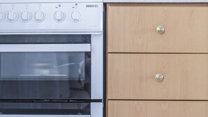 A kitchen with a white Beko oven, wooden cabinets, and a tiled backsplash.