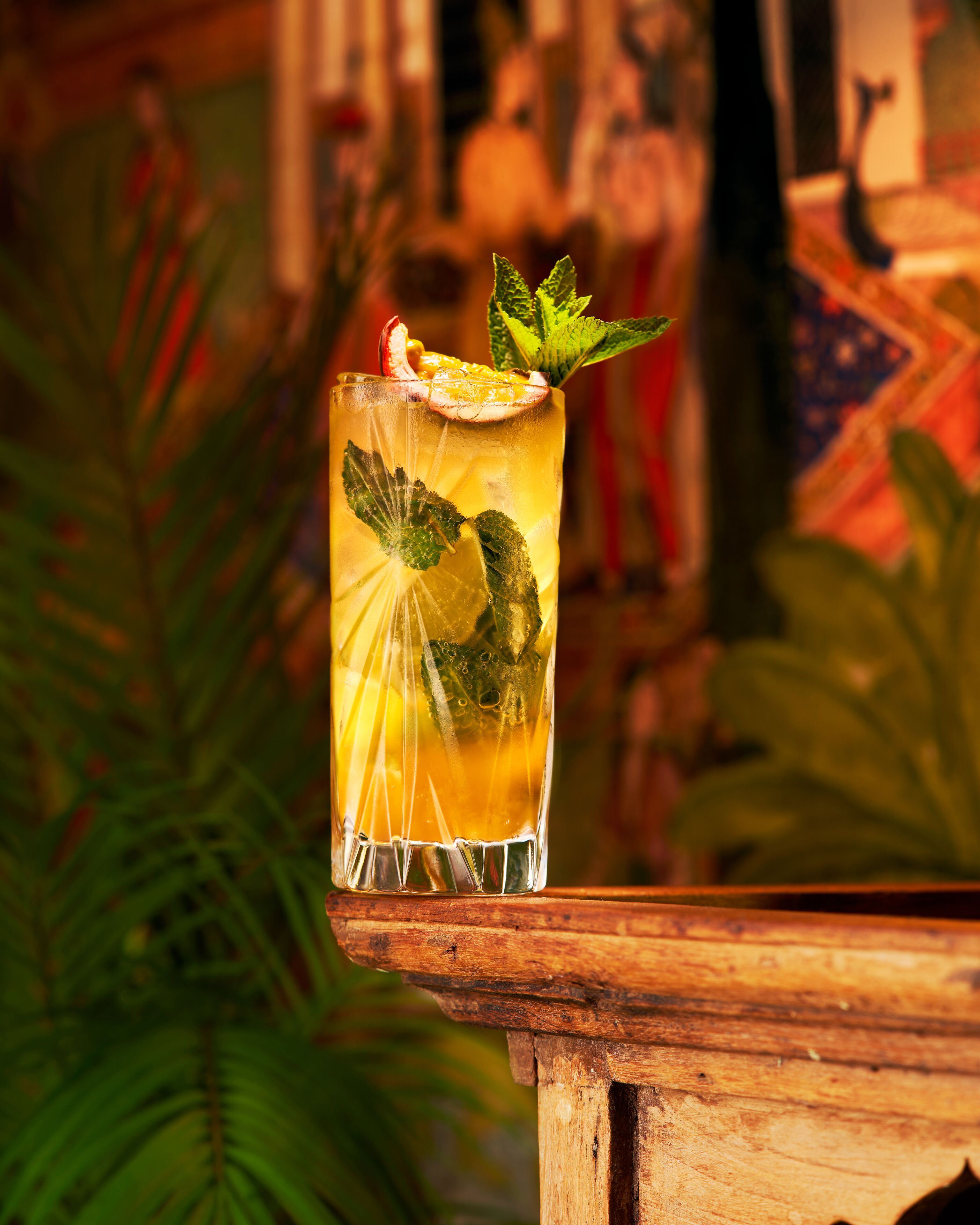 Un verre de cocktail tropical, garni de feuilles de menthe et d’une tranche de citron vert, posé sur une surface en bois.