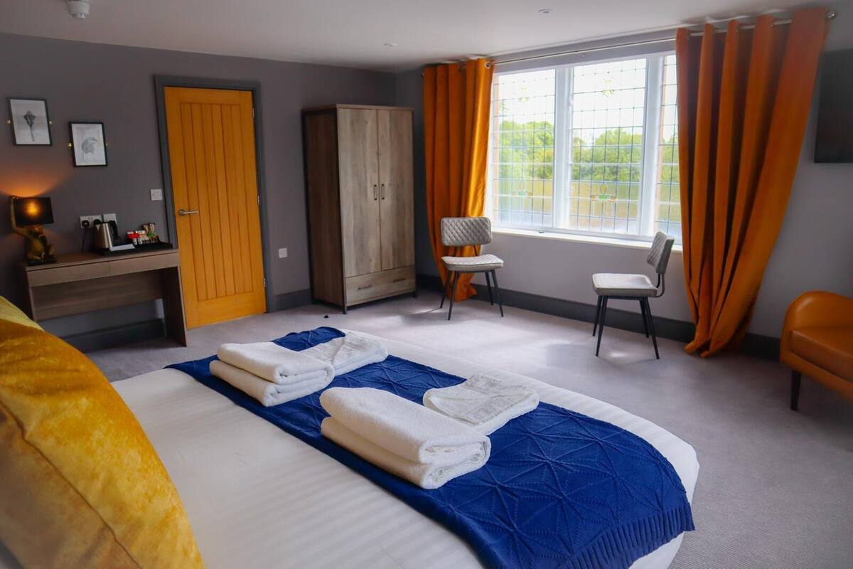 A hotel room with a large bed, a desk, a wardrobe, two chairs, and a window with curtains.