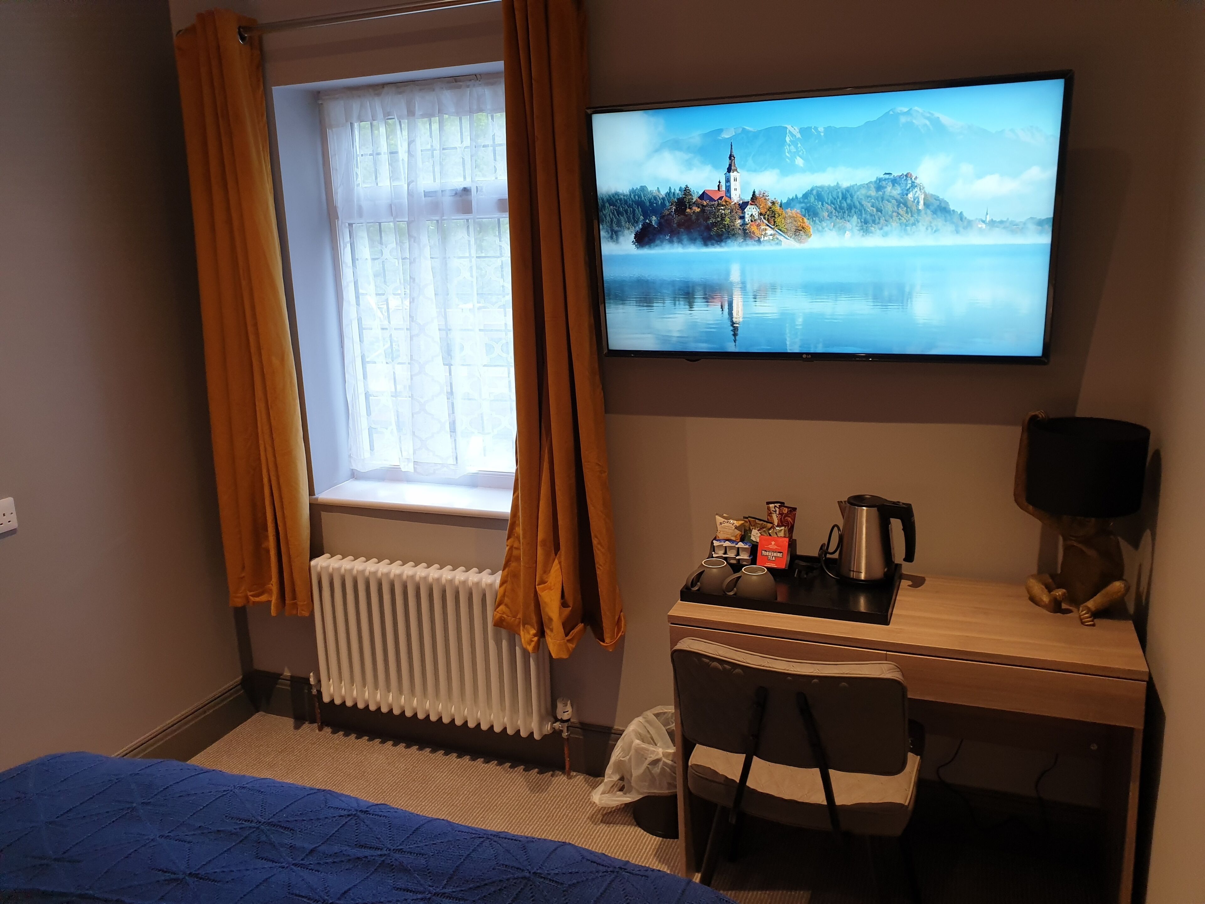 Een hotelkamer met een bed, een bureau met stoel, een televisie en een raam met gordijnen.