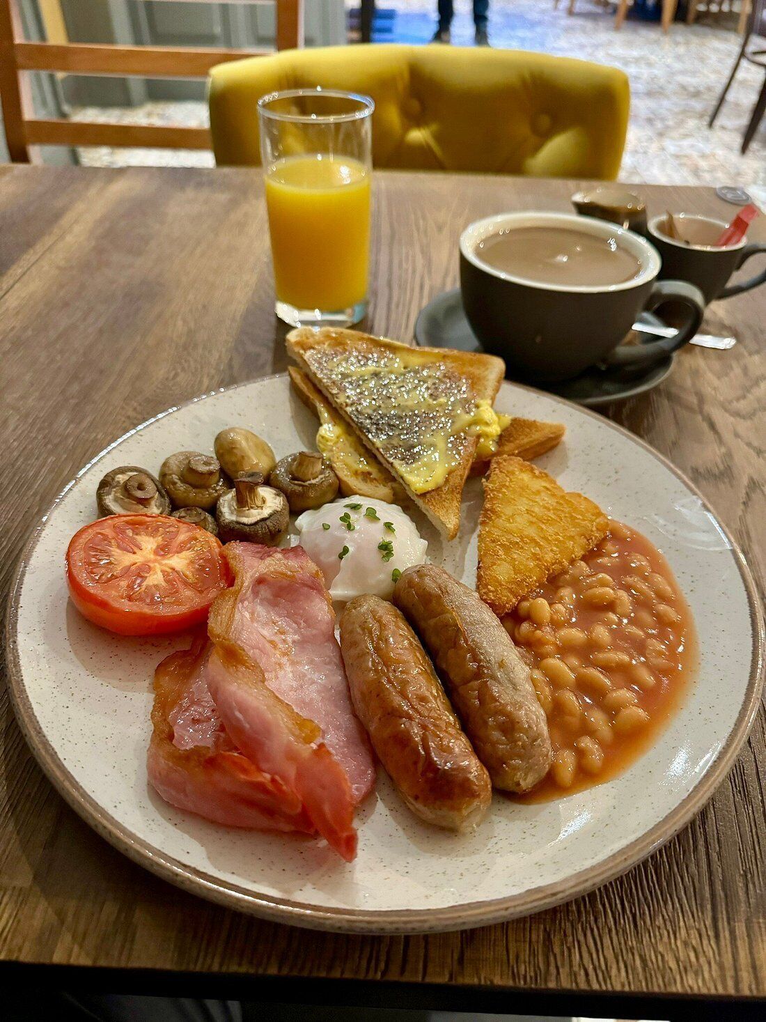 A breakfast plate with eggs, bacon, sausages, mushrooms, beans, and toast.