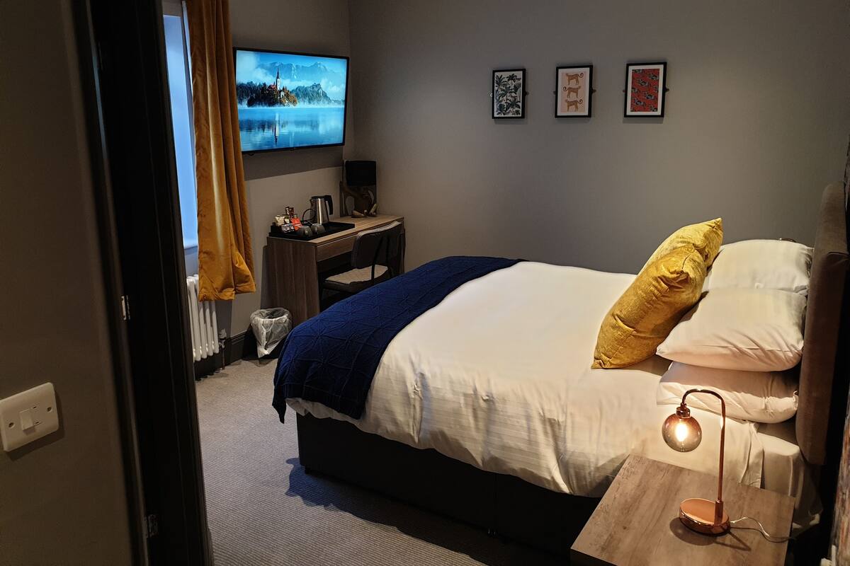A hotel room with a bed, a desk with a computer, a TV, and three framed pictures on the wall.