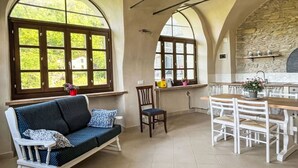 A cozy living room with a sofa, a dining table, and chairs. There are large windows with a view of greenery outside. - Nice apartment for 6 people with WIFI, pool, TV, patio, pets allowed and panoramic view (Prelà Castello)