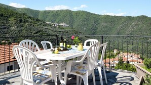 A terrace with a table and chairs, overlooking a mountainous landscape with a village below. - Nice apartment for 6 people with WIFI, pool, TV, patio, pets allowed and panoramic view (Prelà Castello)