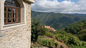 A stone building with a large arched window and a view of a hillside with houses and greenery. - Nice apartment for 6 people with WIFI, pool, TV, patio, pets allowed and panoramic view (Prelà Castello)