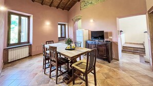 A dining area with a wooden table and chairs, a television, and a stone wall. - Nice apartment for 8 people with pool, WIFI, TV, patio, pets allowed and panoramic view (Prelà Castello)