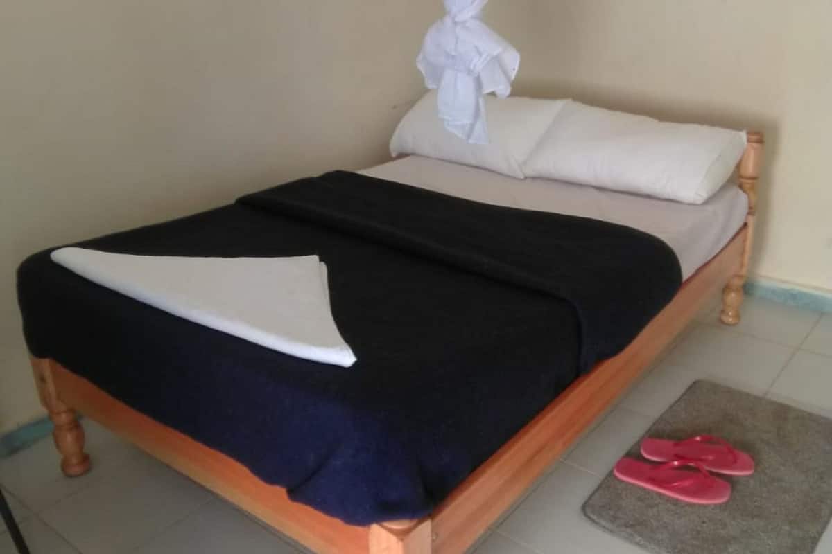 A bed with a canopy, a black and white bedspread, and a pair of pink slippers on a mat.