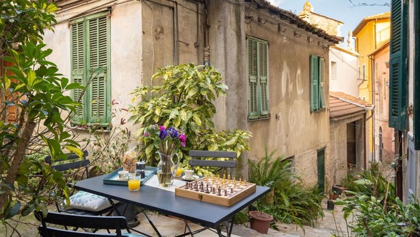 Une terrasse extérieure avec un jeu d’échecs, un vase rempli de fleurs et un plateau avec des boissons.